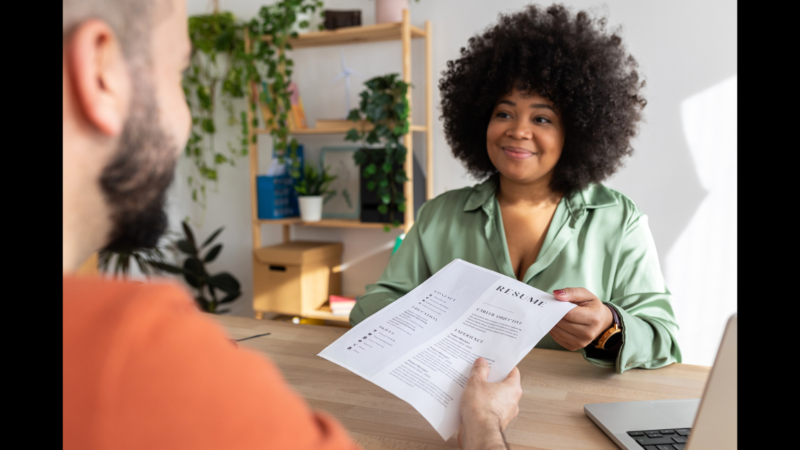 Black woman with afro handing over her resume in job interview in an office for September Surge