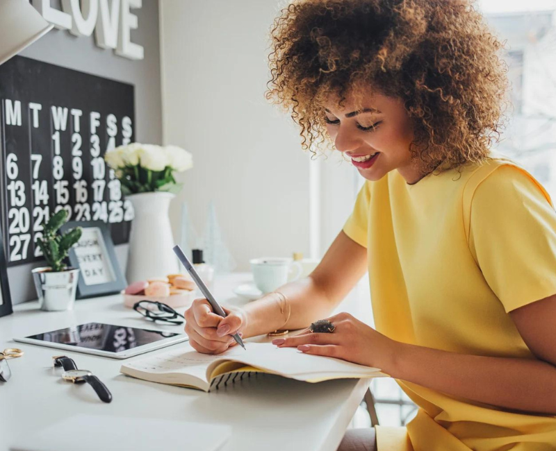 Black woman sitting at desk writing objectives in a notebook