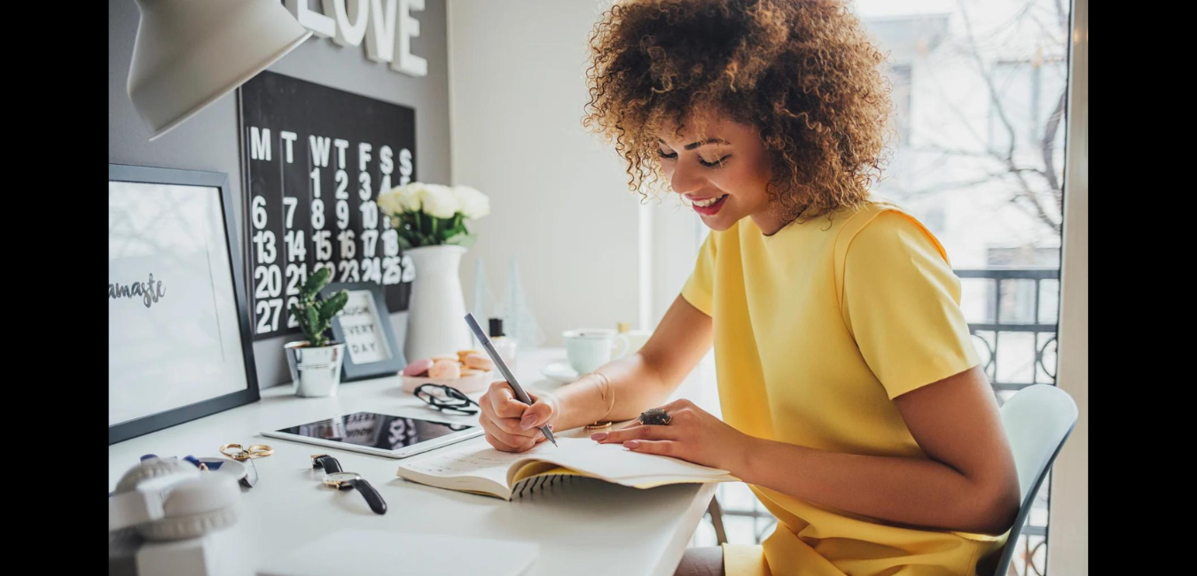 Black woman sitting at desk writing objectives in a notebook