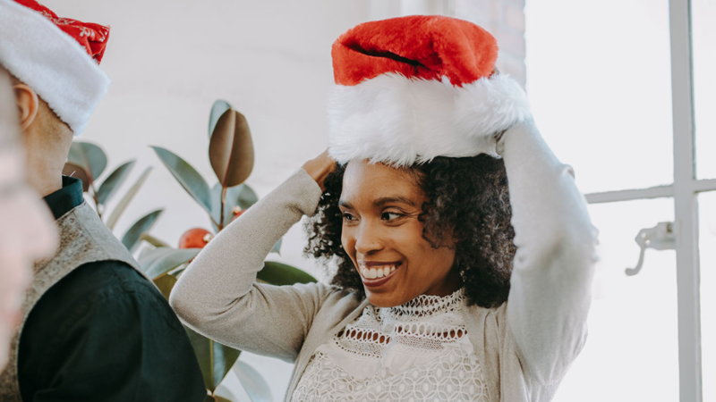 Black woman with red Santa hat at office holiday party Navigate office politics