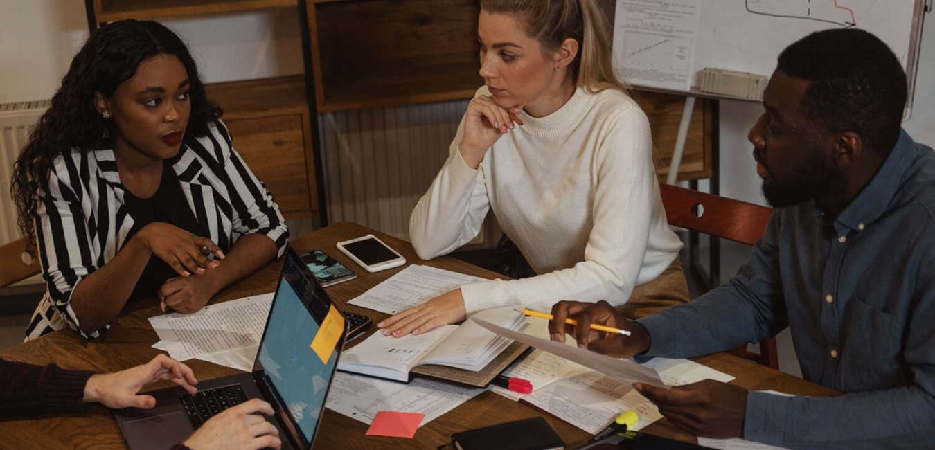 Black woman in work meeting at table with white woman and black man safer workplace article on Divonify