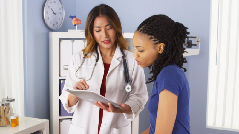 Black woman with doctor looking at paperwork. Need a Break? Here's Exactly How to Take FMLA