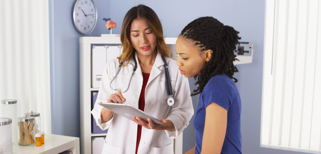 Black woman with doctor looking at paperwork. Need a Break? Here's Exactly How to Take FMLA